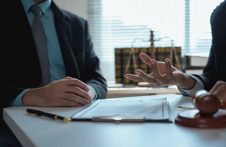Two professionals in suits discussing documents at a desk with legal books and a gavel.