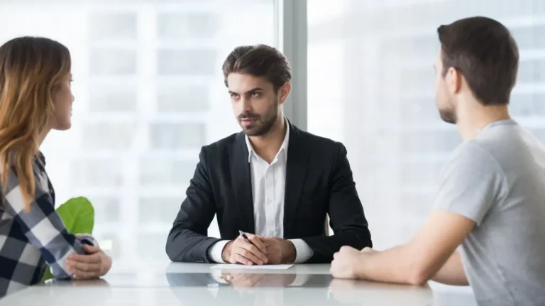 Three professionals engaged in a discussion around a white table in a bright office.