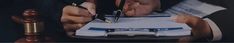 Close-up of hands holding pens and reviewing documents beside a wooden gavel.