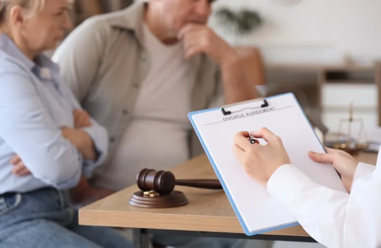 Two individuals sitting at a table with a judge’s gavel and a clipboard titled "Divorce Agreement.