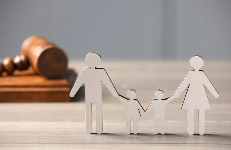 Silver metallic family figurines of two adults and two children on wooden surface with wooden judge gavel in background.