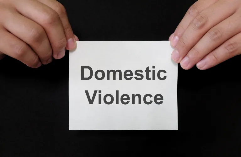 Hands holding a white card with the text "Domestic Violence" on a black background.