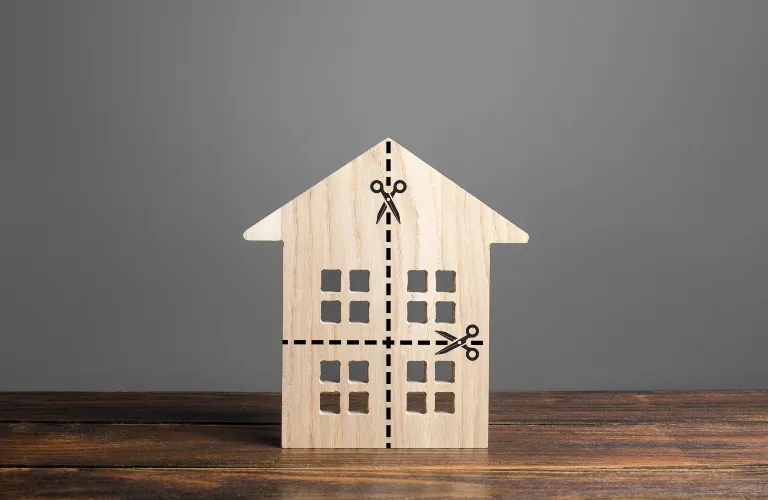 Wooden house model with cut-out windows and black dashed lines with scissors icons on gray background.